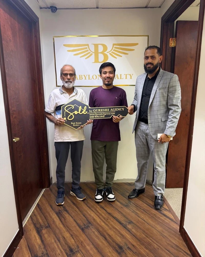 Babylon Realty Managing Broker Sam Qureshi celebrating home closing with buyers holding Sold key sign in Livonia MI